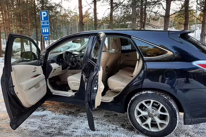 Black luxury SUV with open doors and beige interior parked in snowy lot for private airport transfer
