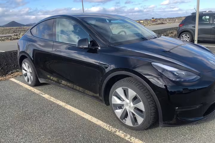 Black Tesla Model Y parked in a lot near volcanic landscape in Iceland