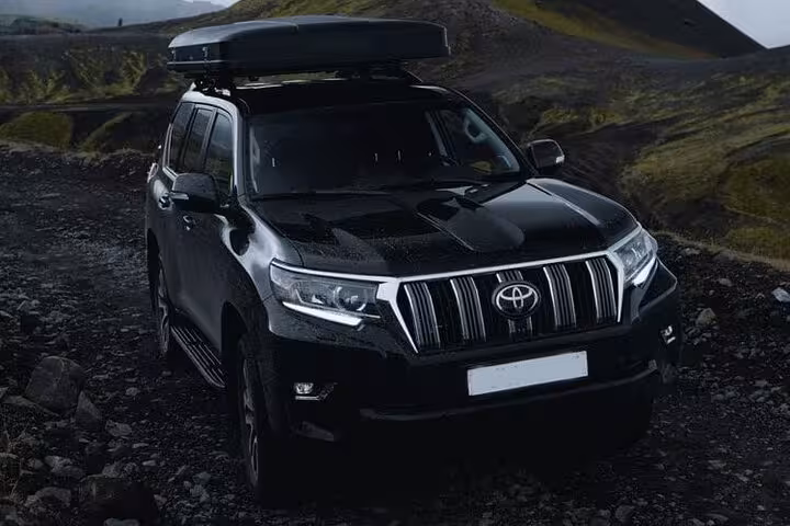 Black Toyota Land Cruiser SUV with roof box on rocky terrain in Iceland highlands