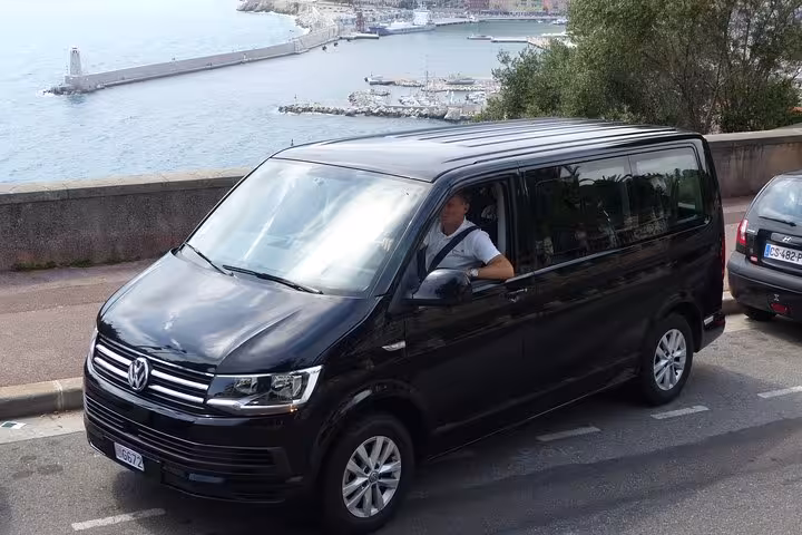 Black Volkswagen Transporter van on French Riviera coastal road with Monaco harbor in background