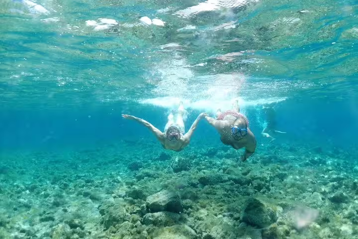 Snorkelers exploring clear turquoise water on Blue Cave & 5 Islands tour, swimming above rocky seabed