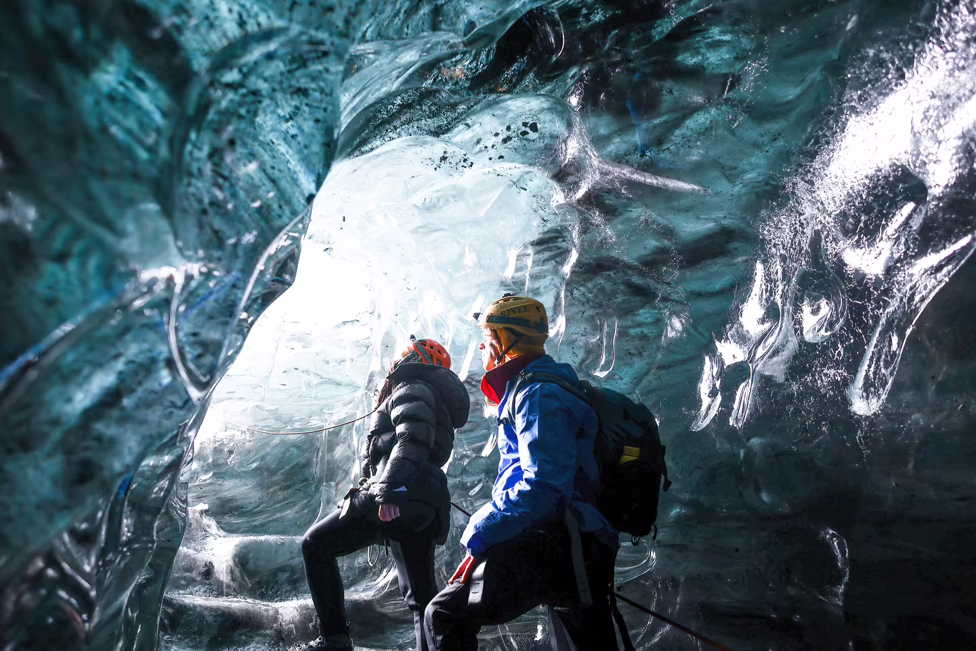 Two explorers with helmets marvel at glowing blue crystal ice cave walls on Vatnajokull Glacier tour