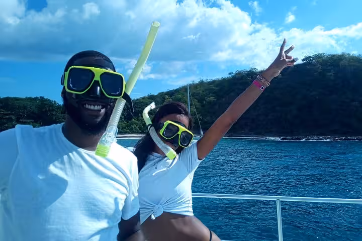 Two snorkelers in vibrant gear pose joyfully on the Blue Dolphin catamaran against a stunning ocean backdrop.