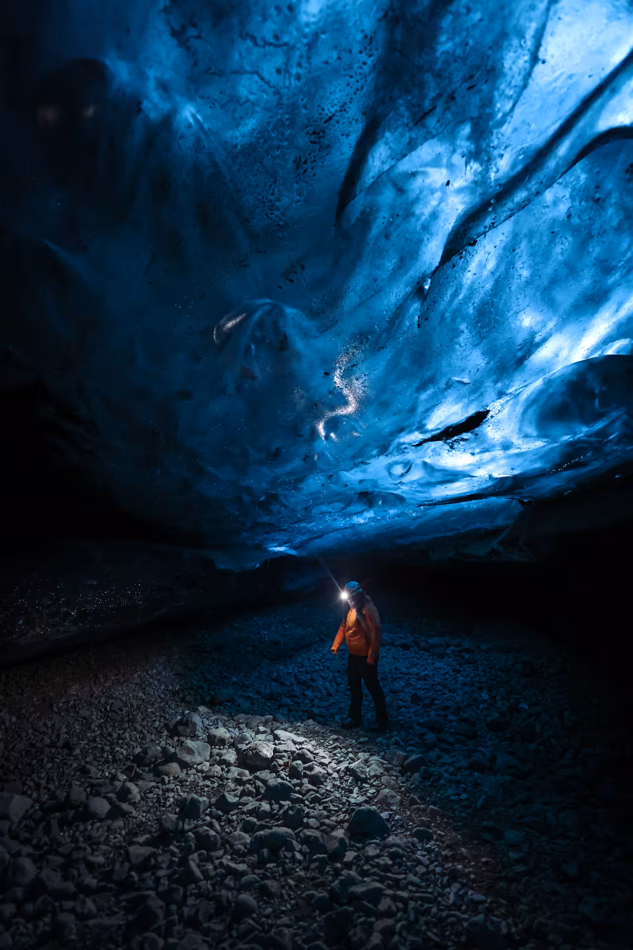 Explorer with headlamp standing inside a stunning blue glacial ice cave during Iceland winter adventure tour