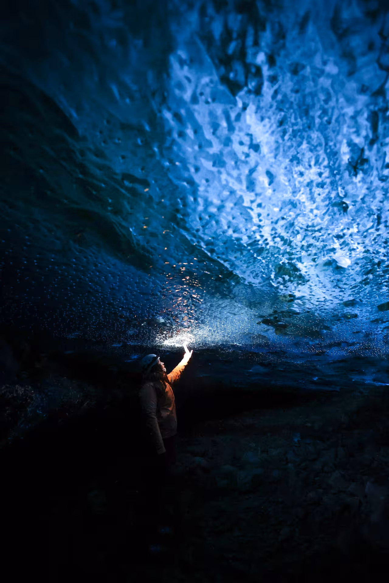 Adventurer touching glowing blue glacial ice cave ceiling on a guided Iceland winter glacier tour