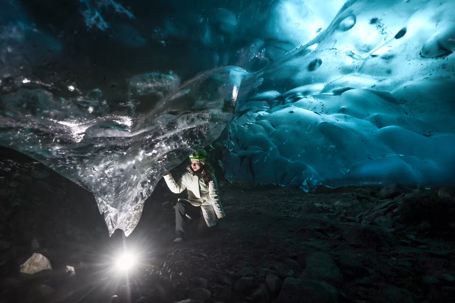 Explorer with headlamp crouching inside a stunning blue glacier ice cave on Eggtrip winter glacier hike adventure
