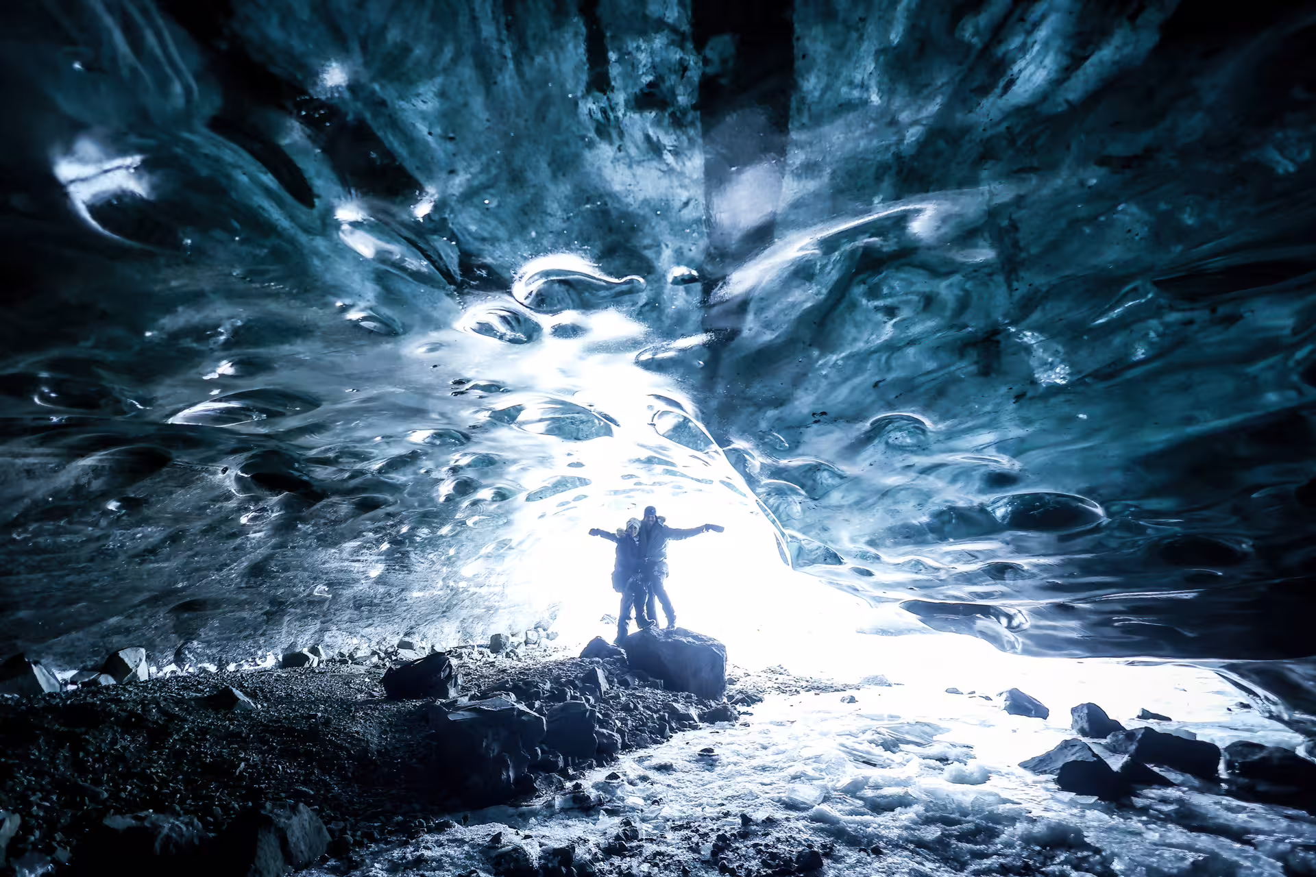Two adventurers celebrating inside a breathtaking blue glacier ice cave illuminated by glowing natural light in Iceland