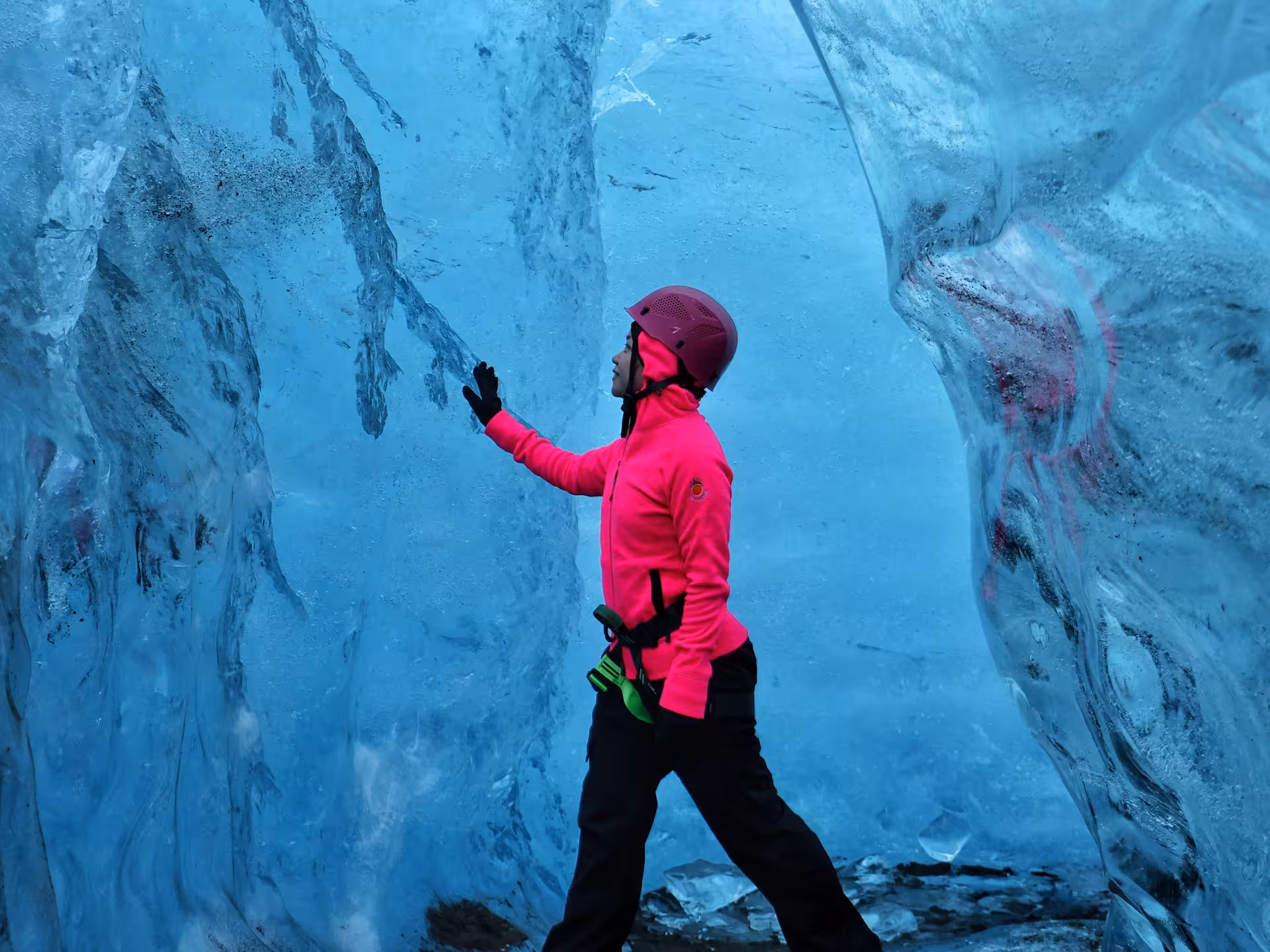 Explorer in pink jacket touching blue ice cave walls on Iceland glacier tour