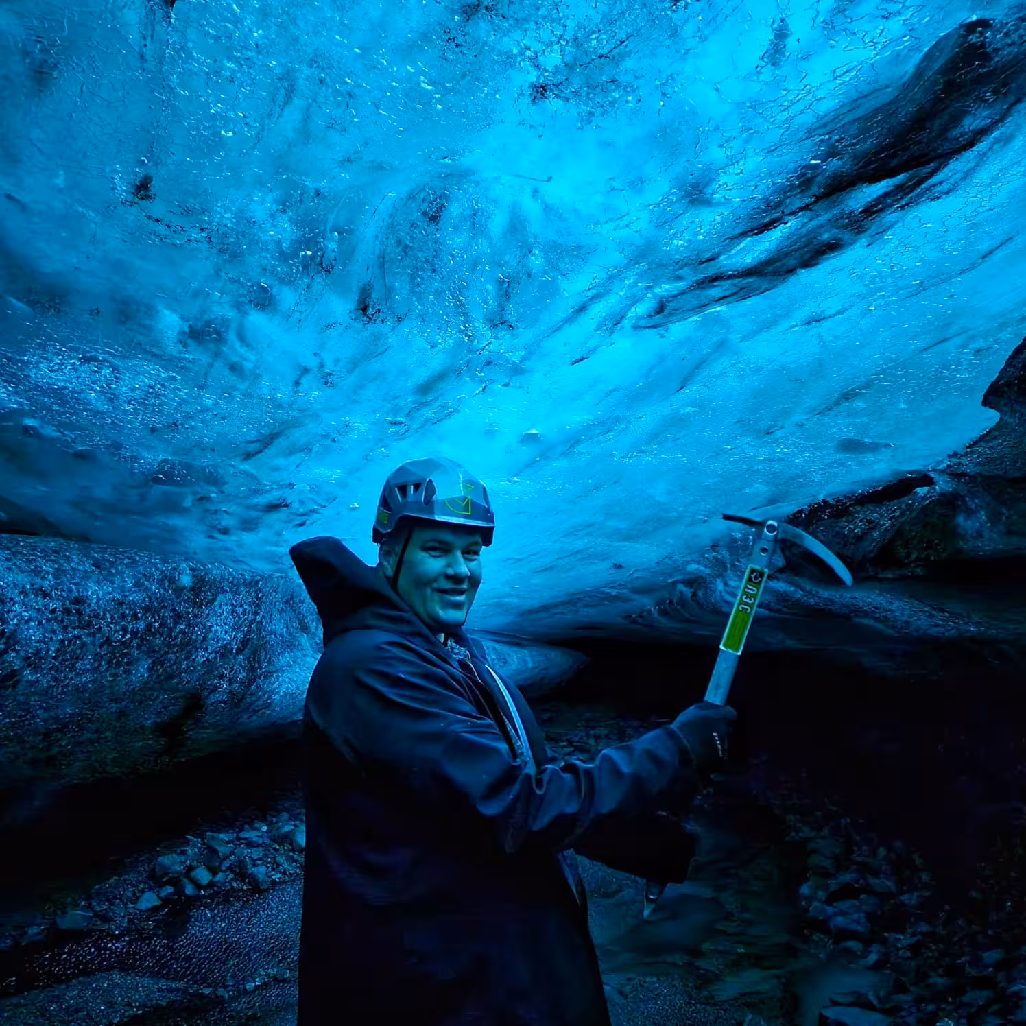 Smiling explorer with ice axe and helmet inside stunning blue ice cave in Iceland