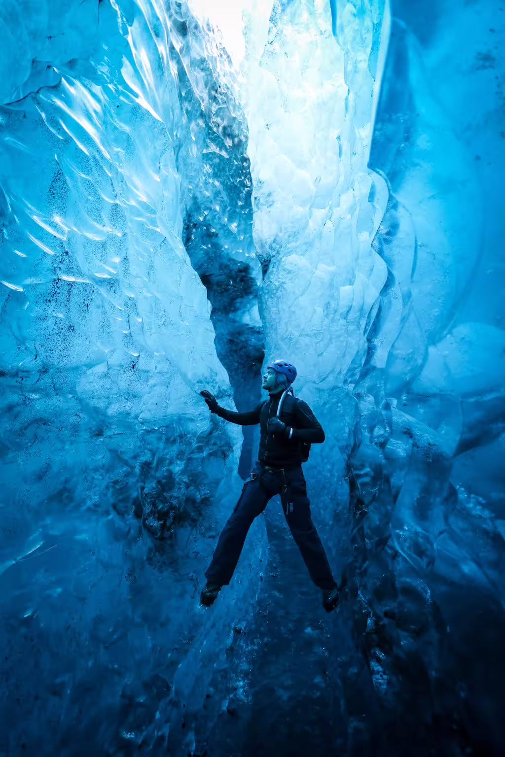 A helmeted adventurer navigates a narrow glowing blue ice cave passage on a private glacier photoshoot tour.