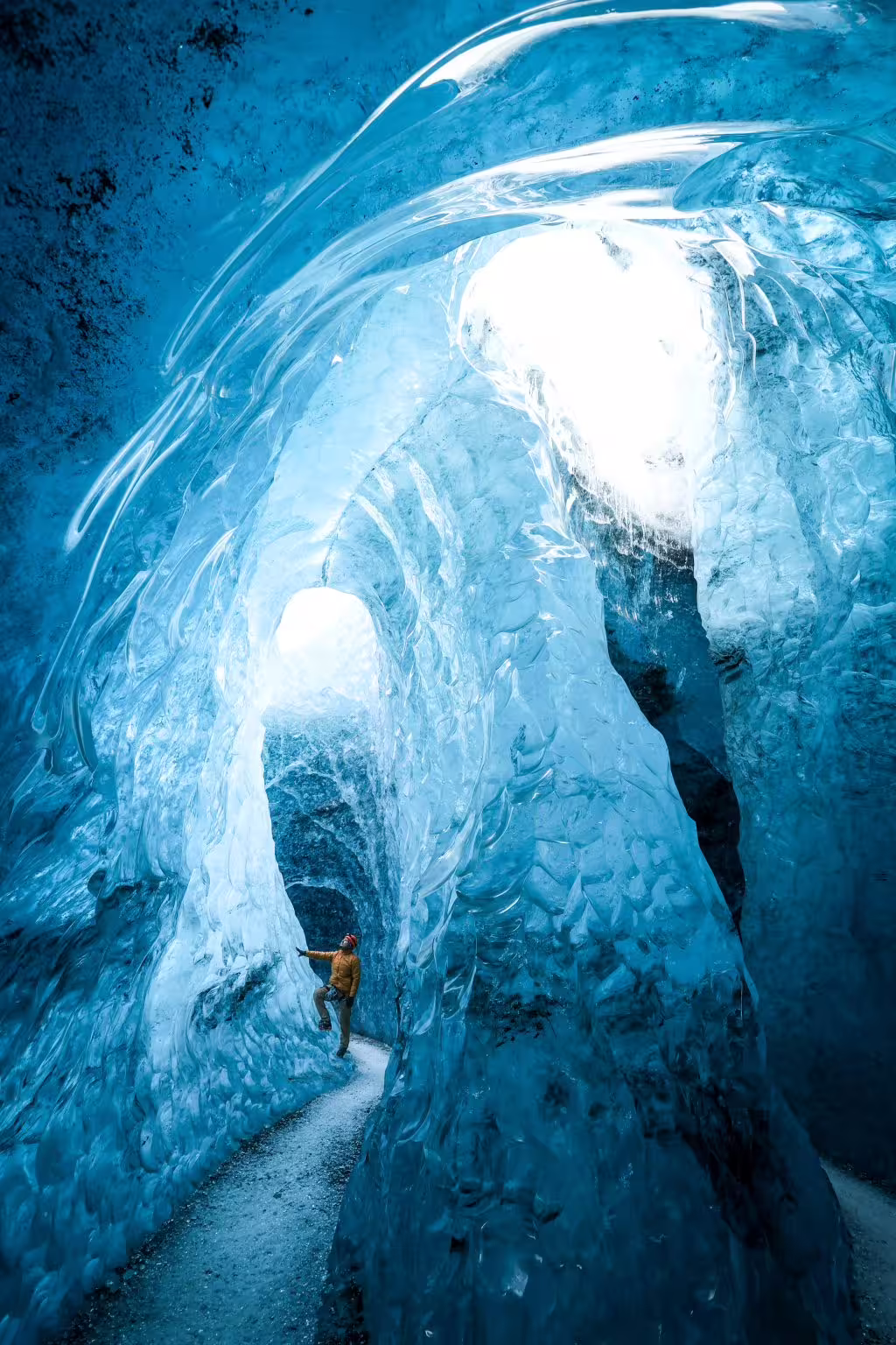 Adventure climber in yellow jacket gazes up at breathtaking blue ice cave tunnels on a private glacier tour