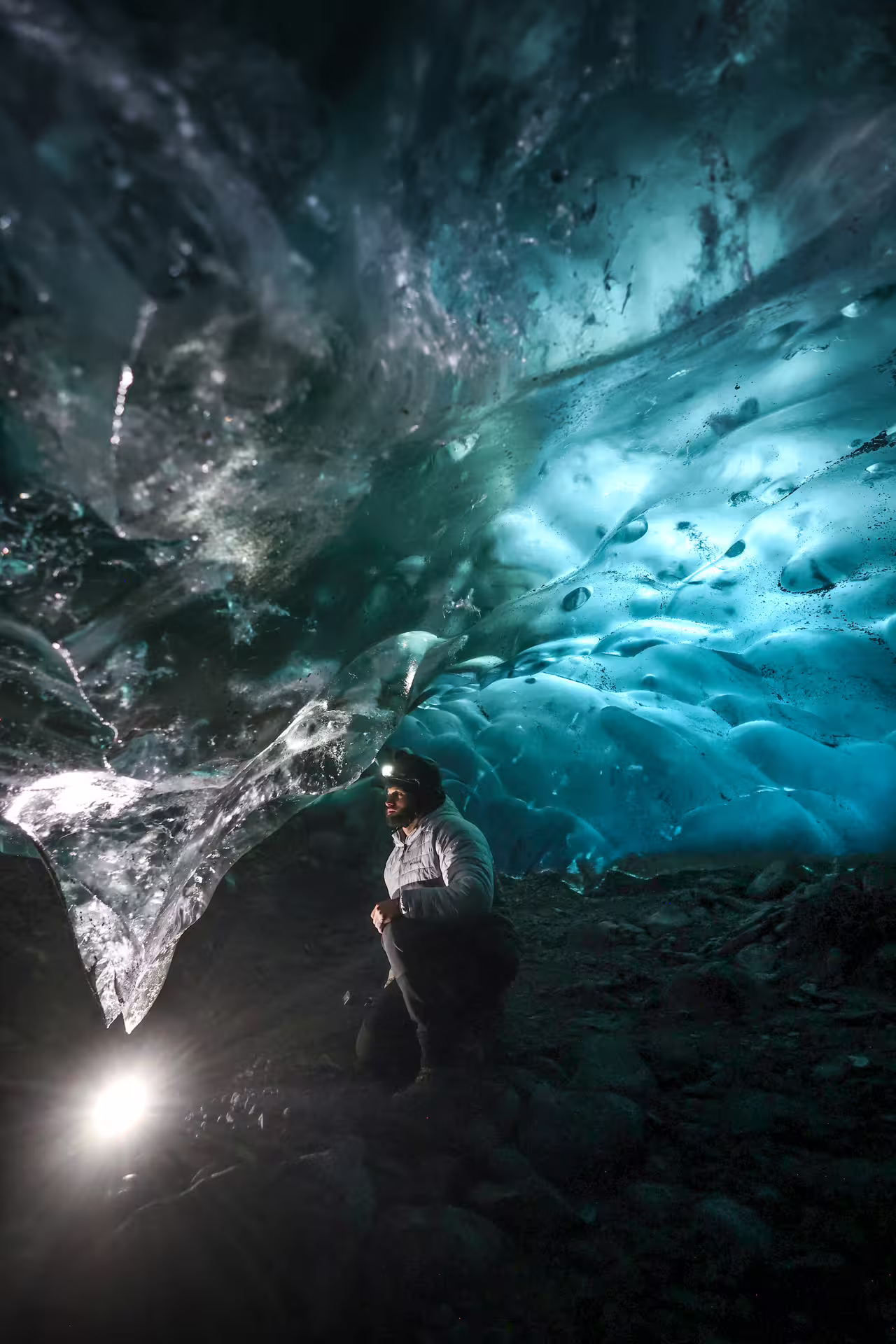 Explorer with headlamp marvels at glowing blue ice cave ceiling on Eggtrip winter glacier hike adventure