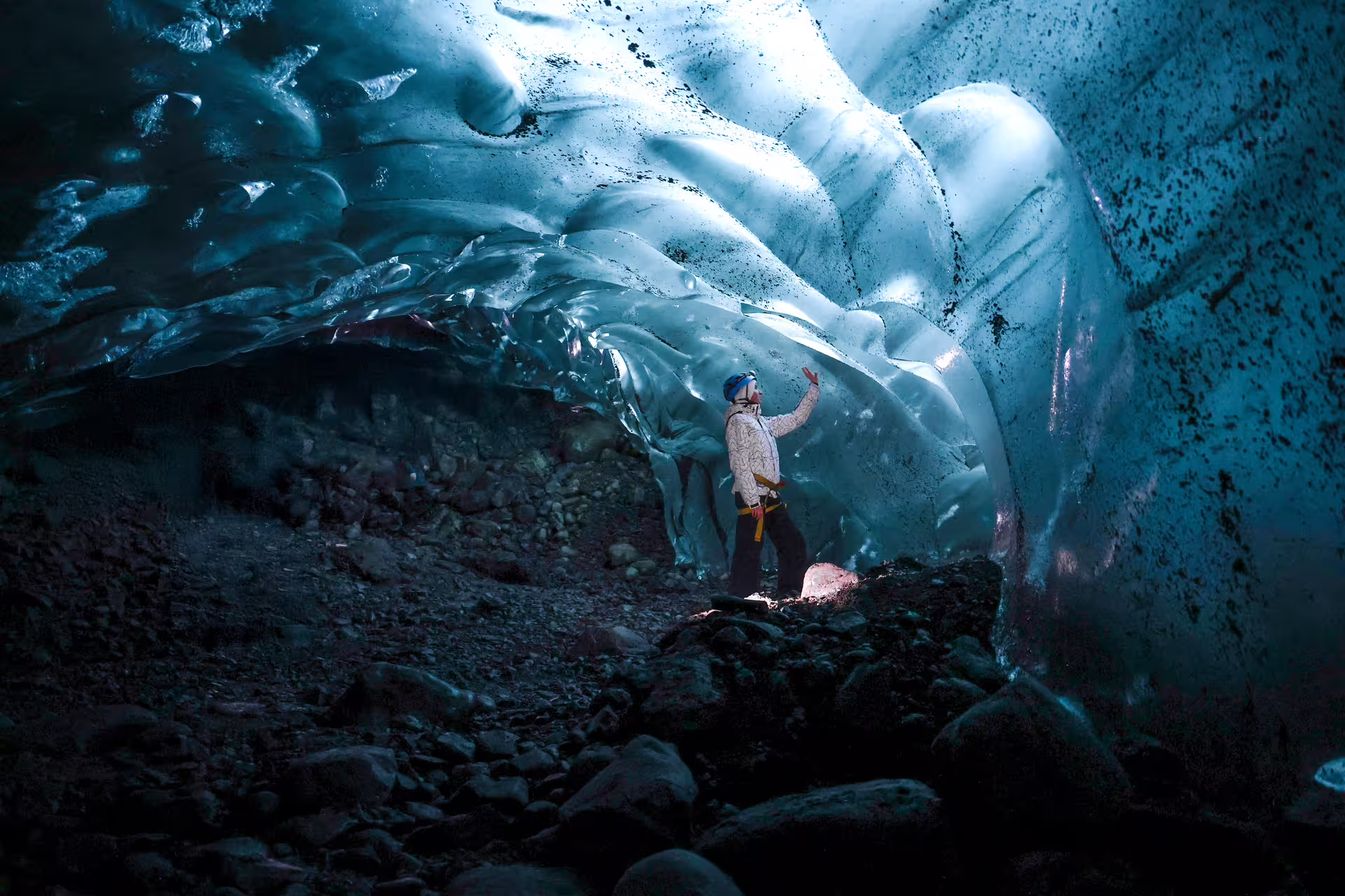 Hiker in safety gear touching glowing blue glacial ice cave walls during Eggtrip winter glacier hike Iceland tour