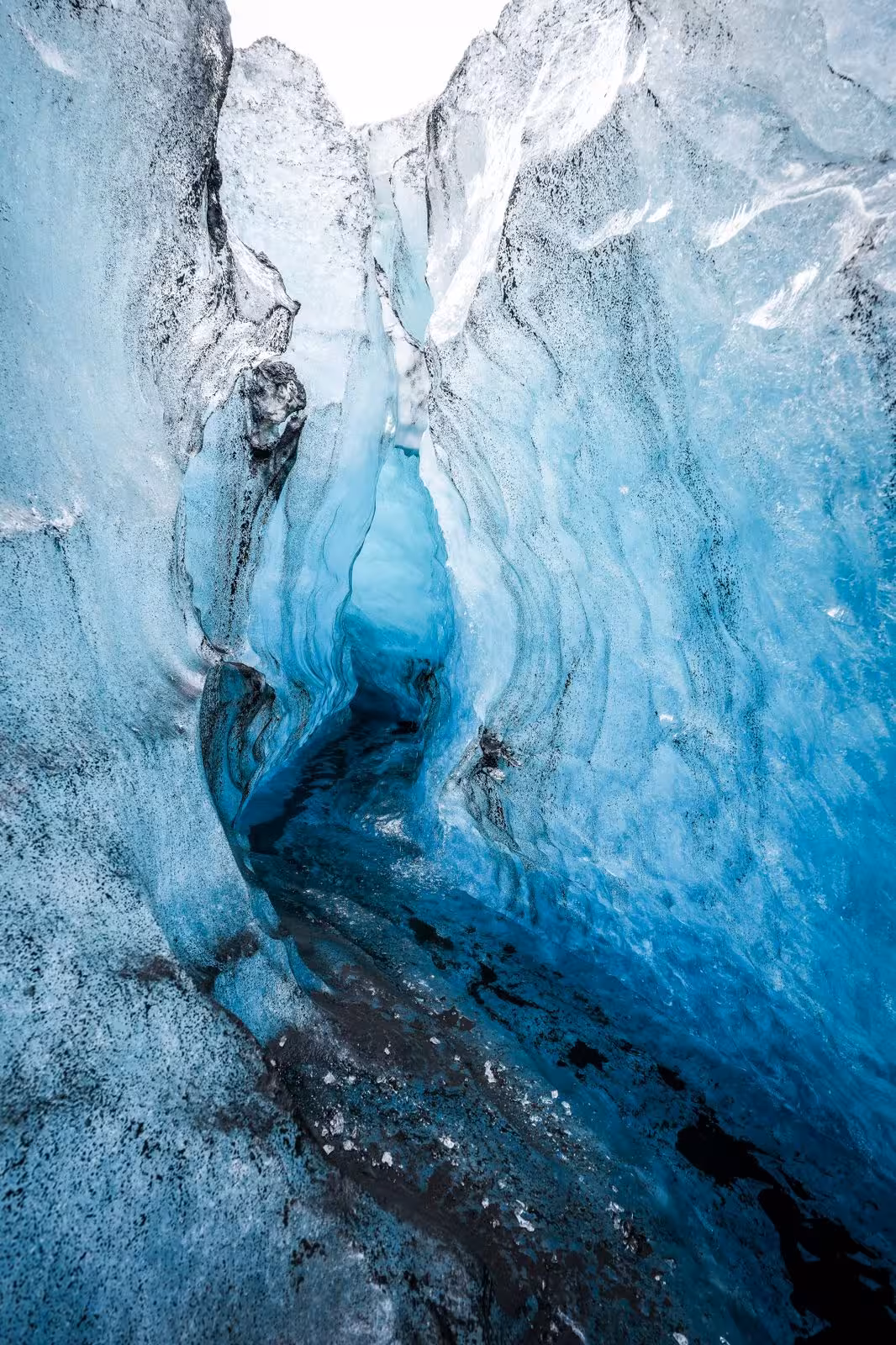 Blue glacial ice cave with swirling layers and dark rock formations inside an Icelandic glacier