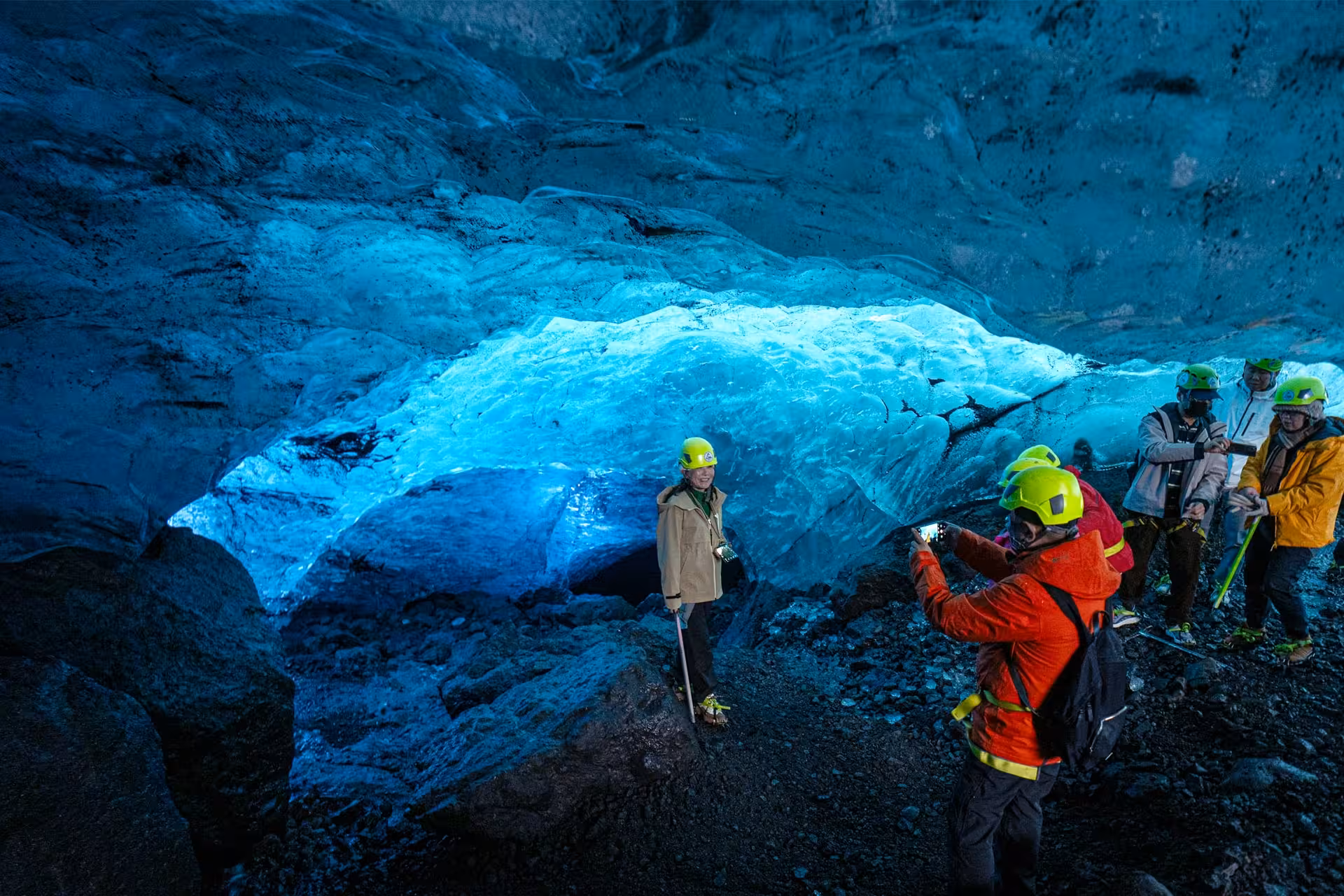 Tour group with yellow helmets exploring a glowing blue ice cave on an Iceland glacier hike