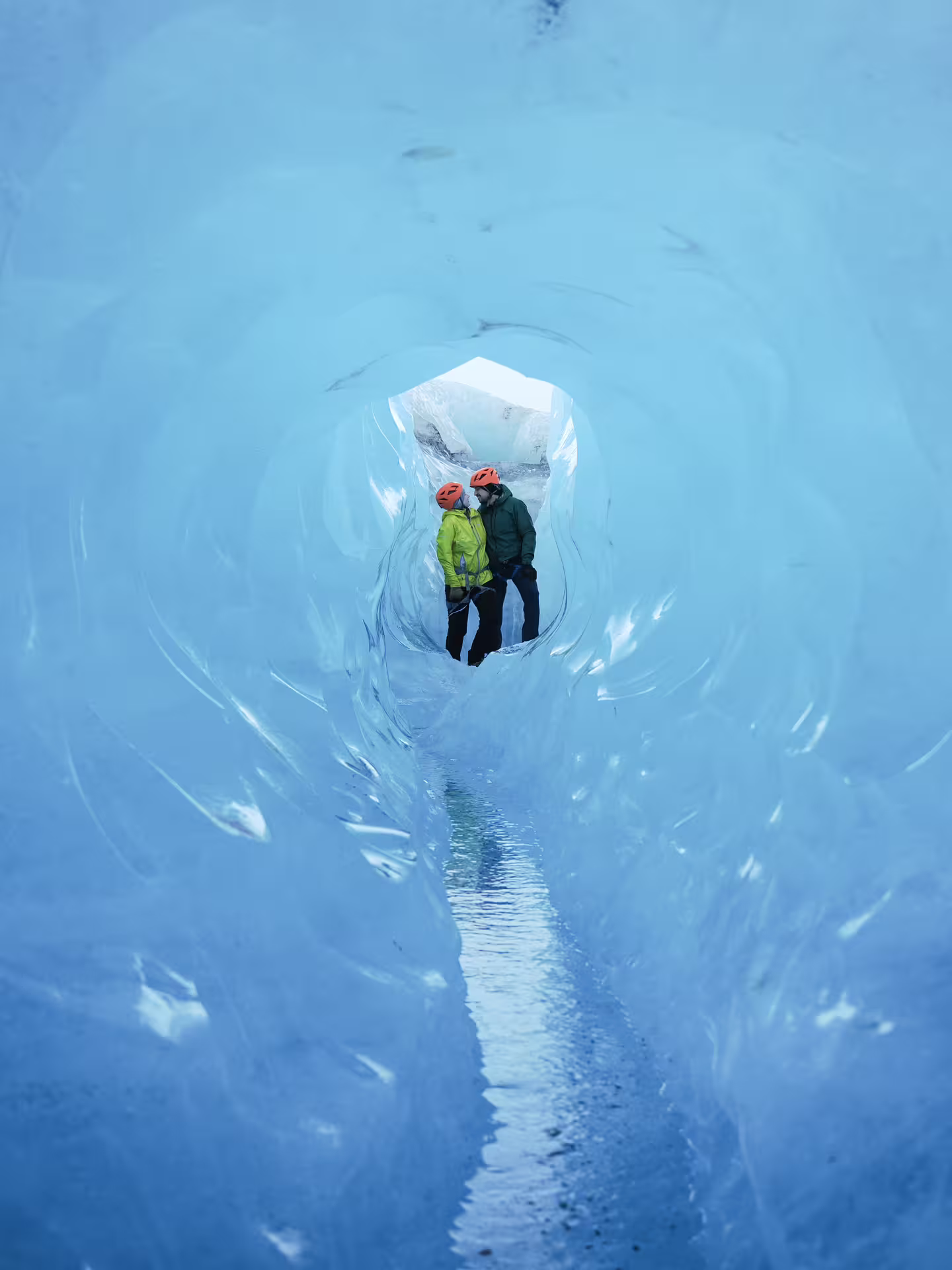 Two adventurers in safety helmets explore a breathtaking blue ice cave tunnel during a winter glacier hike and ice cave tour.