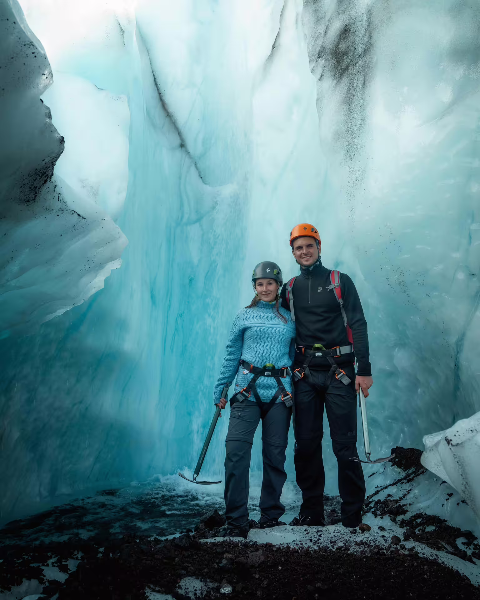 Two hikers in helmets and harnesses pose inside a stunning blue glacial ice cave on a private glacier hike tour.
