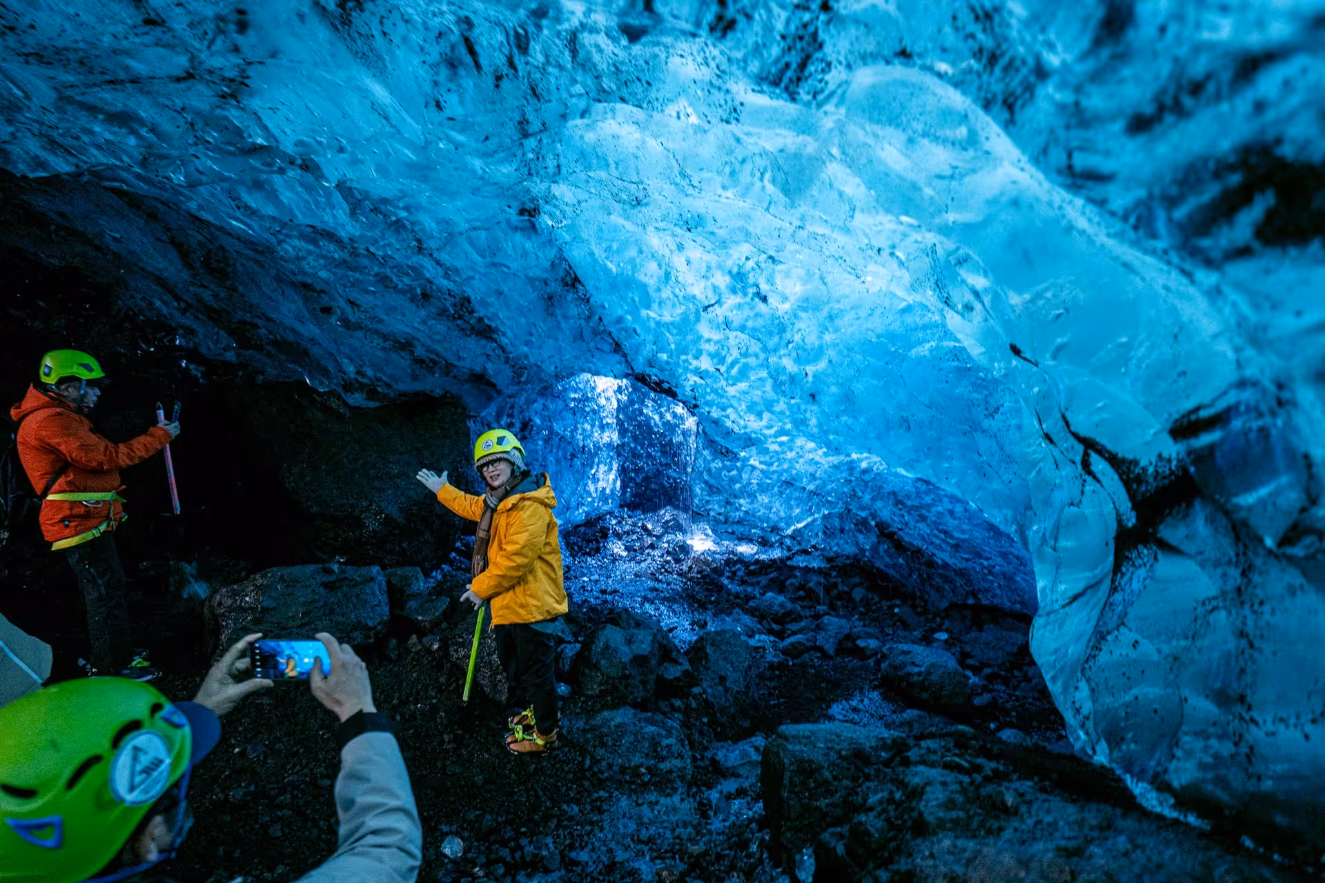 Tourists in safety helmets exploring a glowing blue ice cave on a glacier hike tour in Iceland