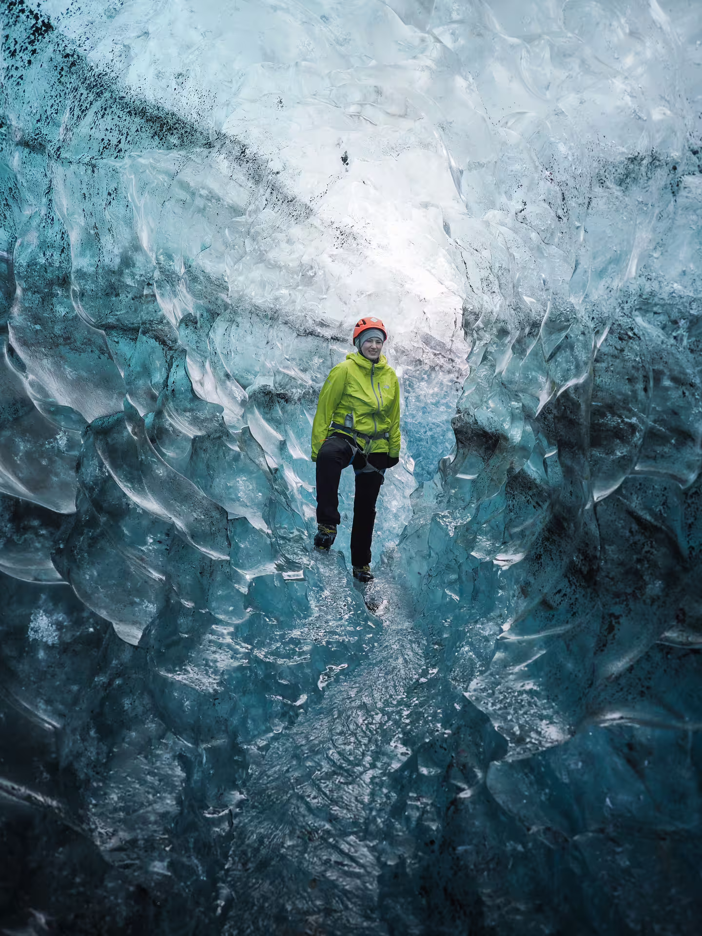 Smiling hiker in orange helmet walks through stunning blue ice cave tunnel on Eggtrip glacier adventure tour