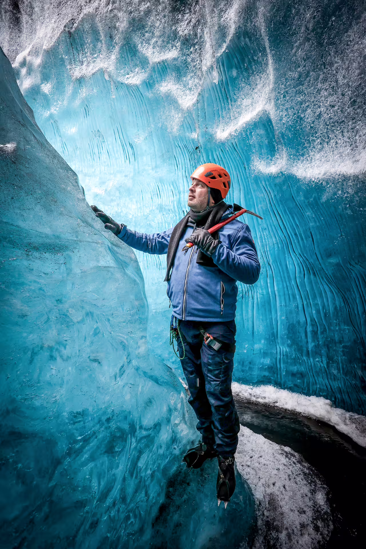 A helmeted climber with an ice axe explores a stunning blue ice cave on a private glacier hiking tour