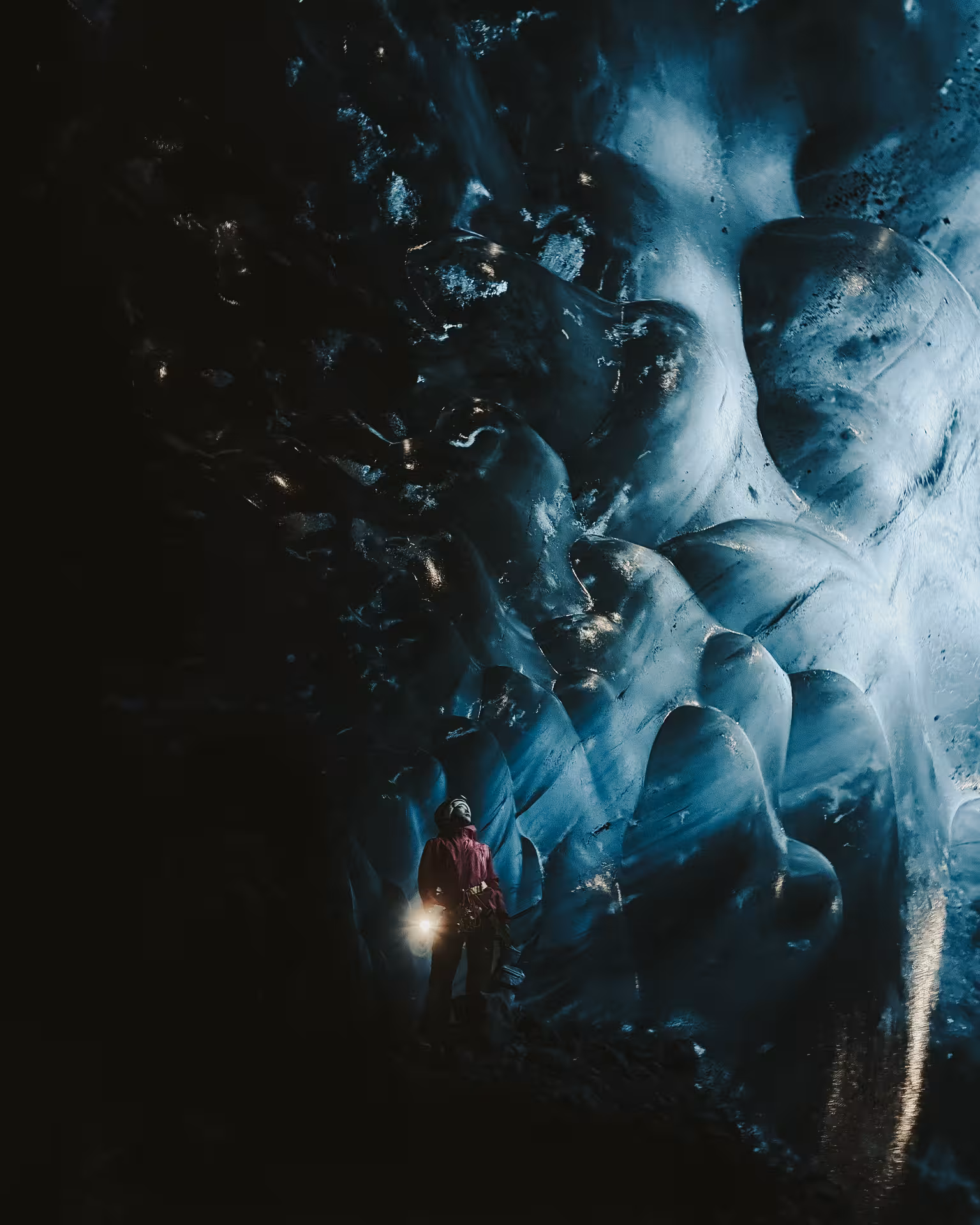 Explorer with lantern standing in awe inside a dramatic blue ice cave on a full-day Iceland glacier tour