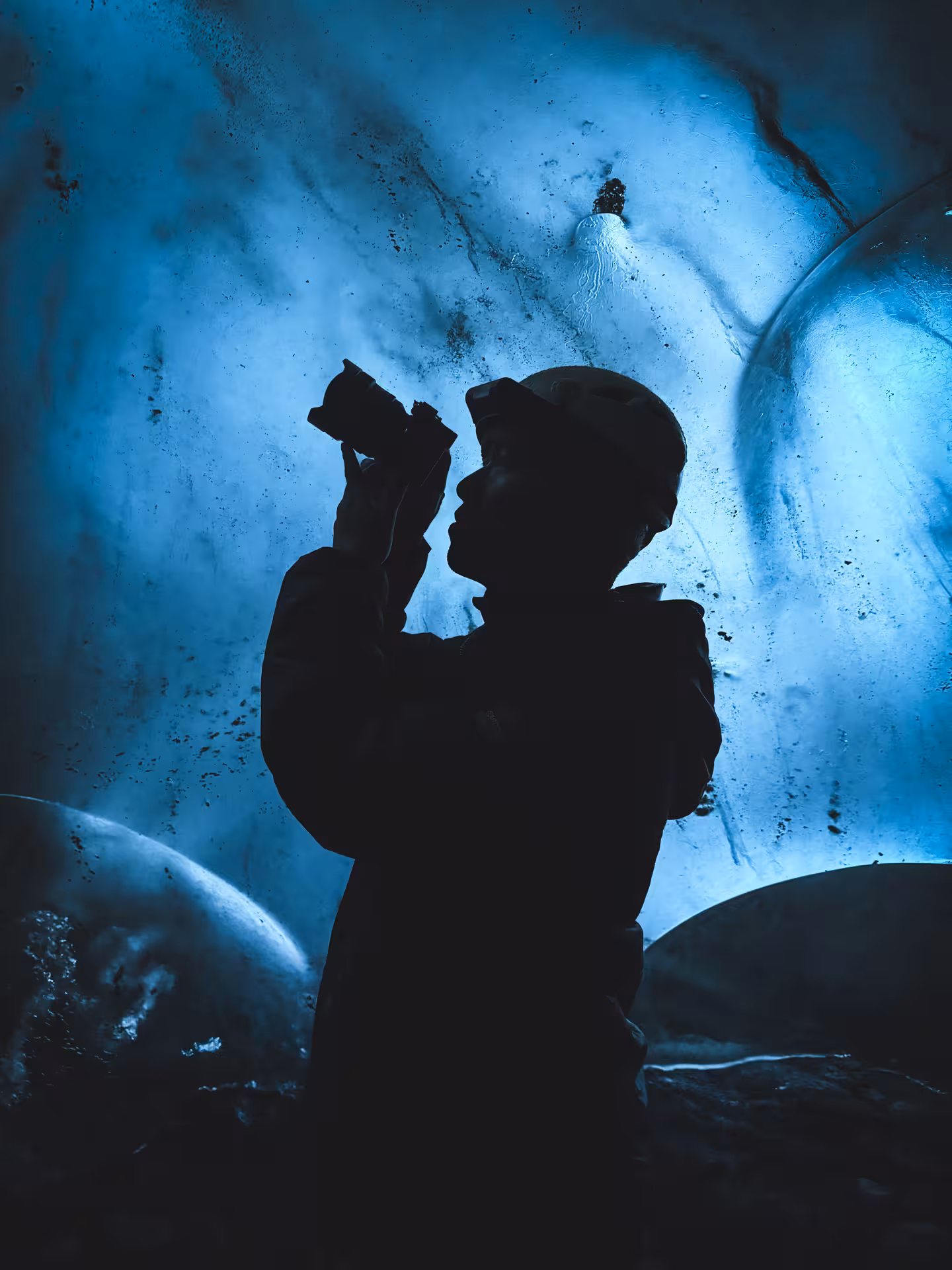 Tourist silhouette photographing stunning blue ice formations inside an Iceland glacier cave adventure tour