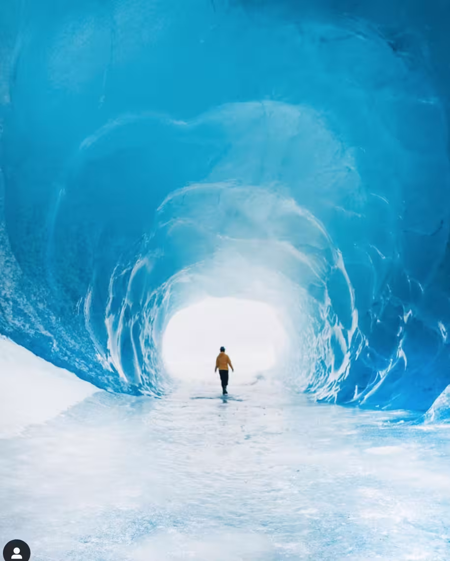 Explorer walking through a glowing turquoise blue ice cave tunnel on an Iceland glacier adventure tour