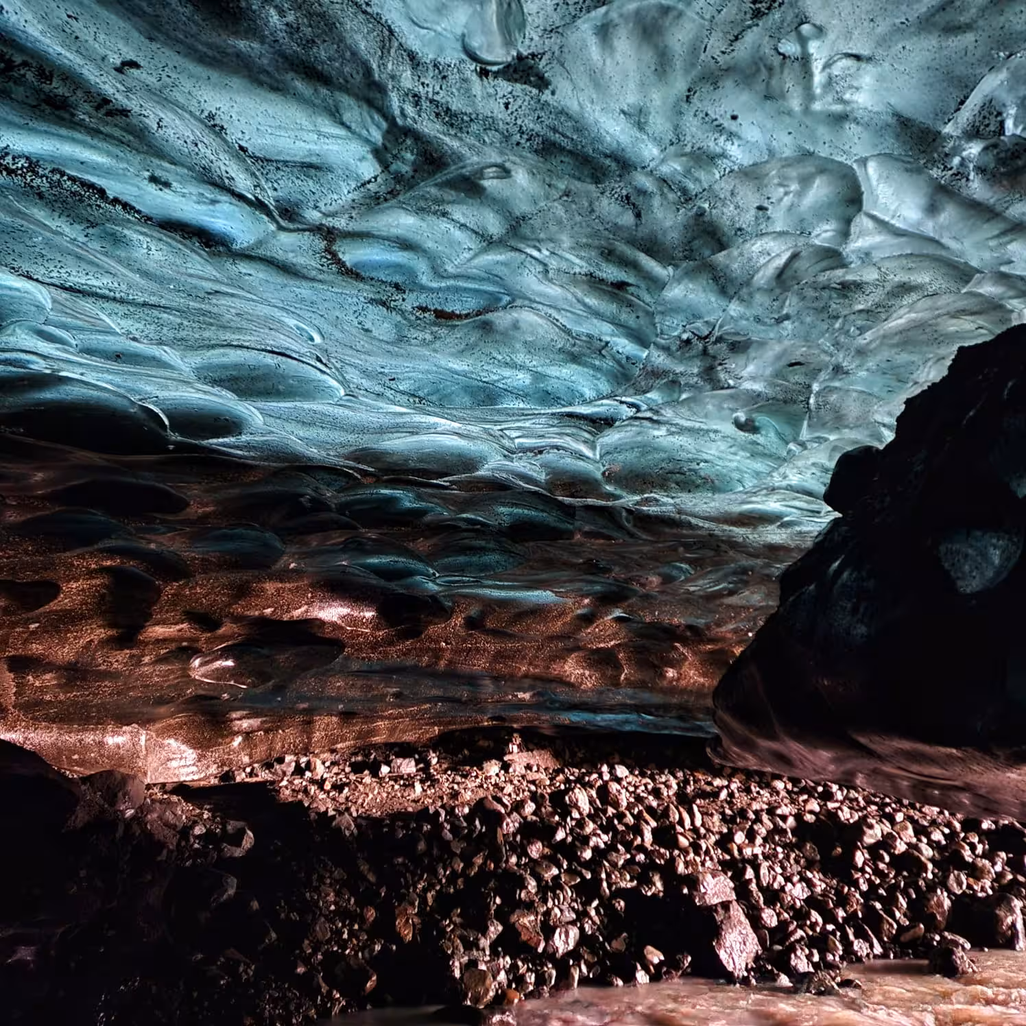 Interior of a blue ice cave in Iceland with glowing turquoise glacier ceiling and rocky floor