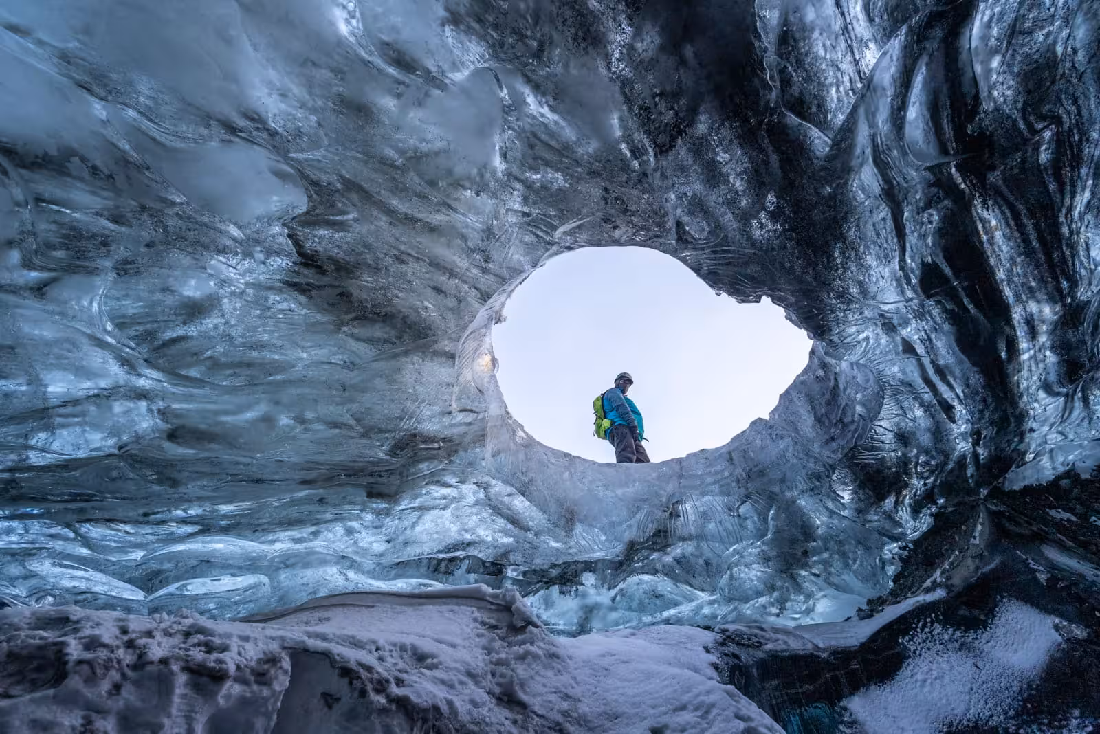 Explorer standing at entrance of blue ice cave on Icelandic glacier viewed from inside