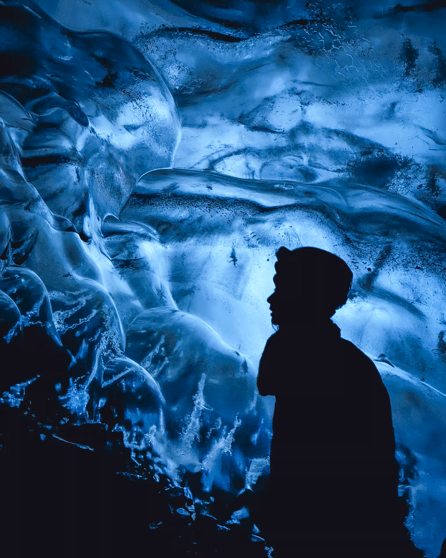 Silhouette of a traveler gazing up at stunning blue ice cave walls on a full-day Iceland glacier tour