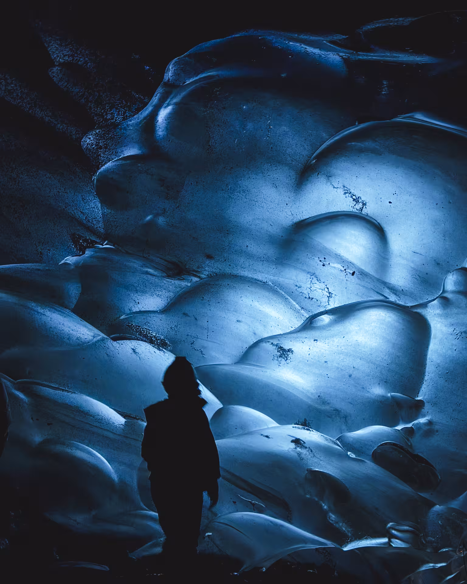 Solo explorer gazing up at mesmerizing blue glacial ice formations deep inside an Iceland ice cave tour