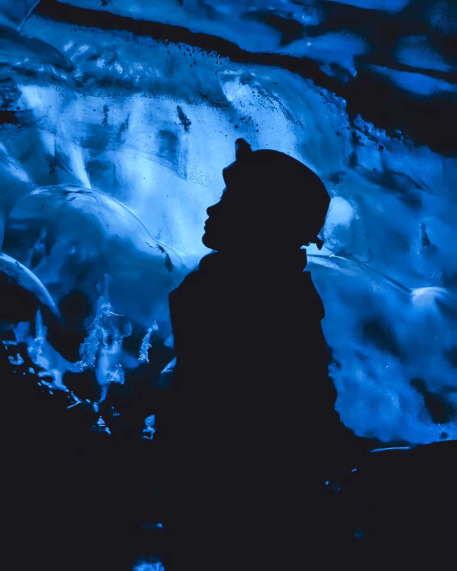 Silhouette of a traveler gazing up at glowing blue ice cave walls on an Iceland glacier tour