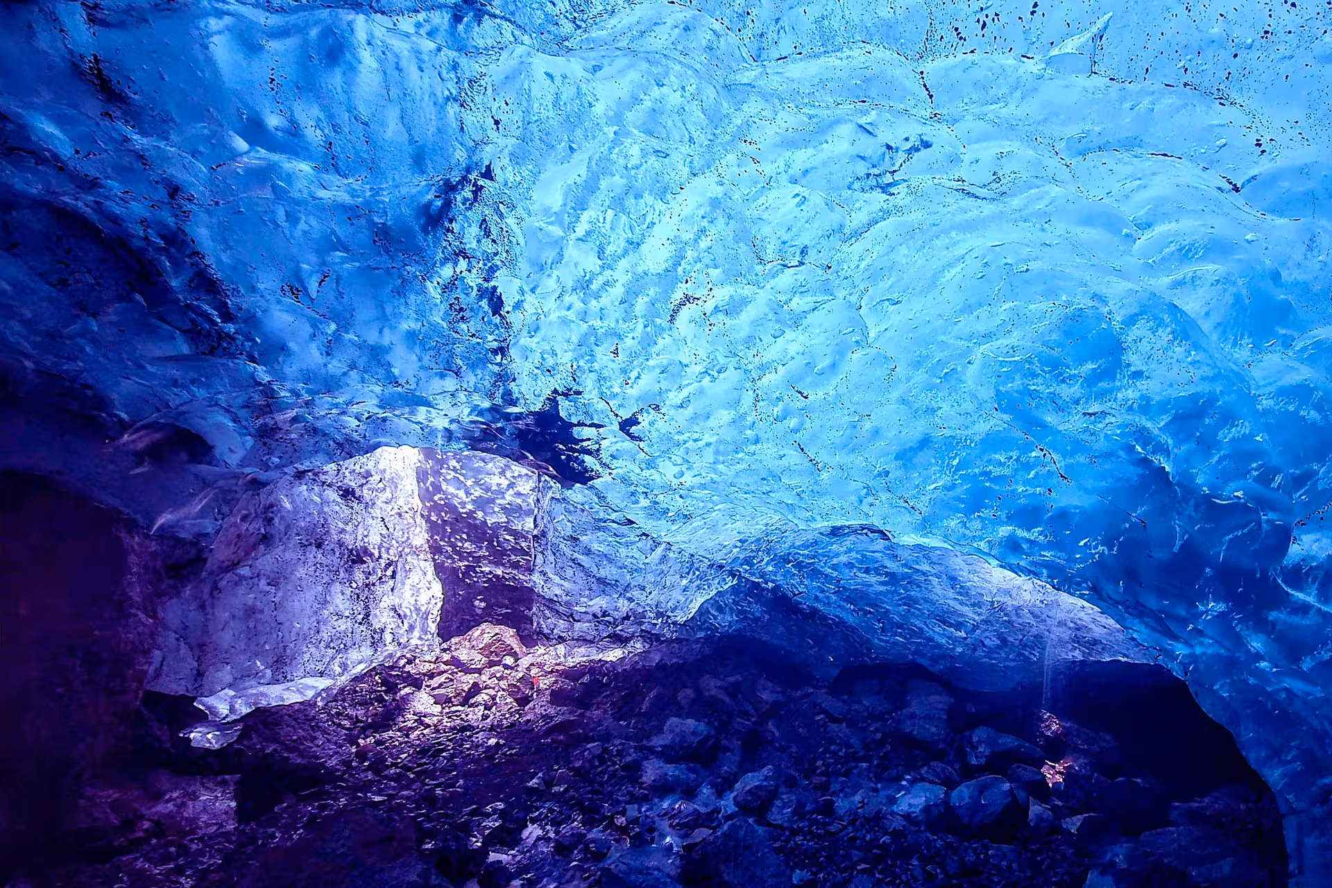 Glowing blue ice cave ceiling with rocky floor on Iceland glacier hike tour