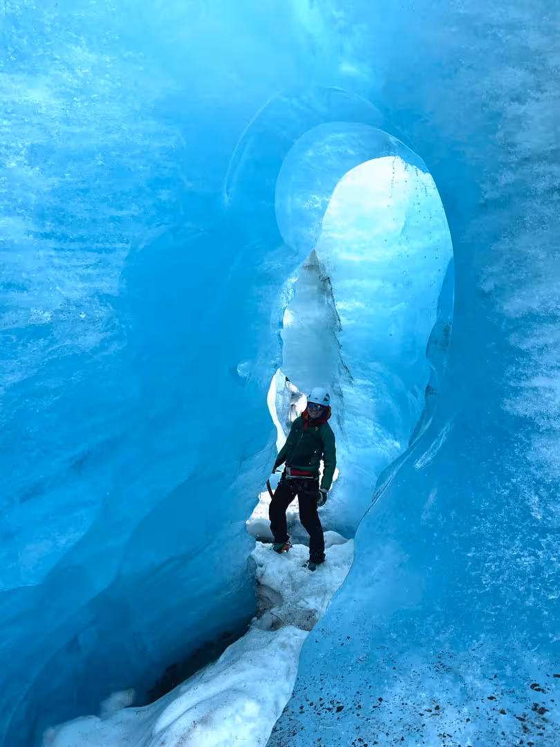 Explorer in helmet and harness standing inside glowing blue ice cave on Solheimajokull glacier Iceland