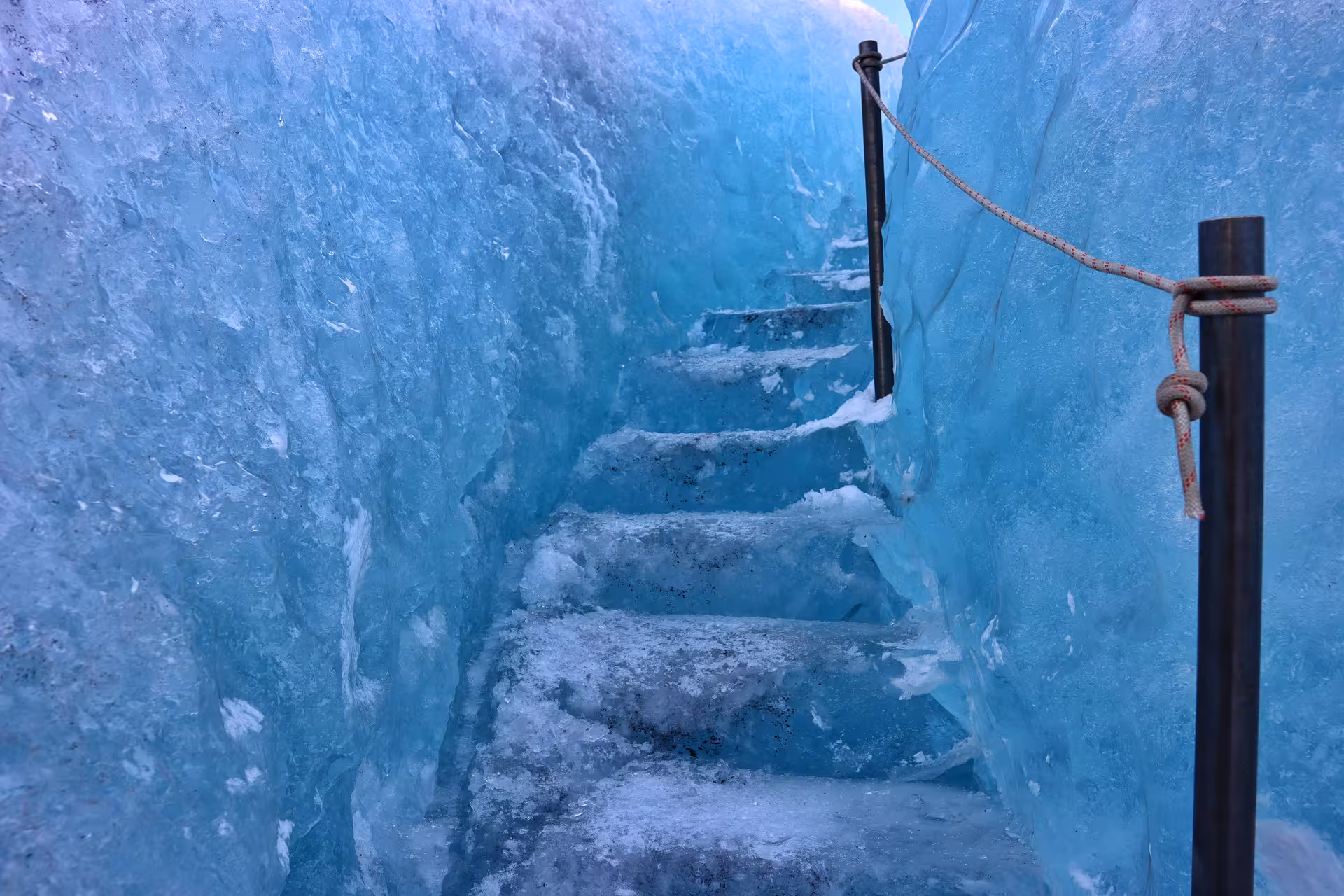Ice stairs carved into blue glacier with rope handrail inside an Iceland ice cave