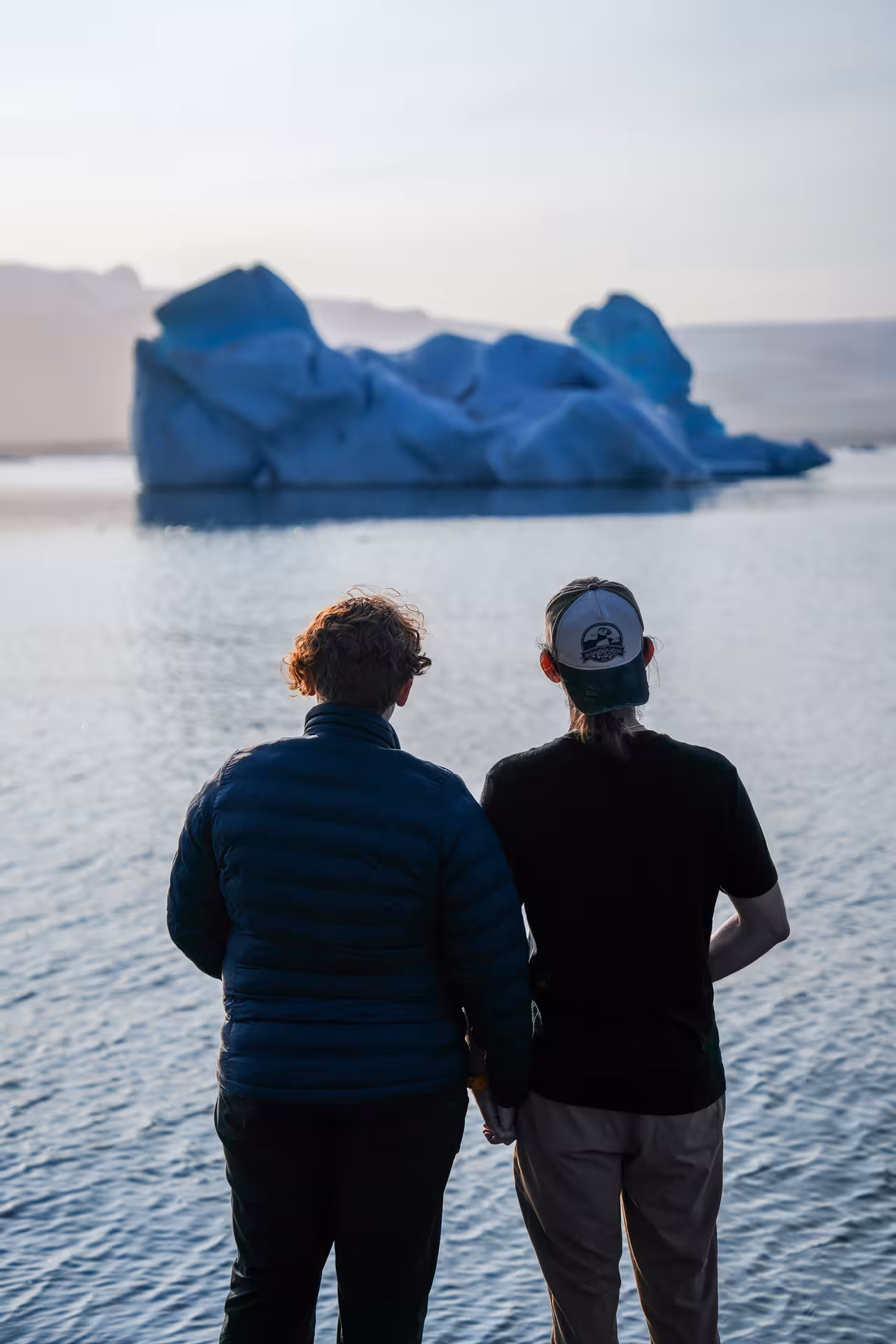 Two travelers admire a glowing blue iceberg on Iceland's Jokulsarlon glacier lagoon zodiac boat tour.