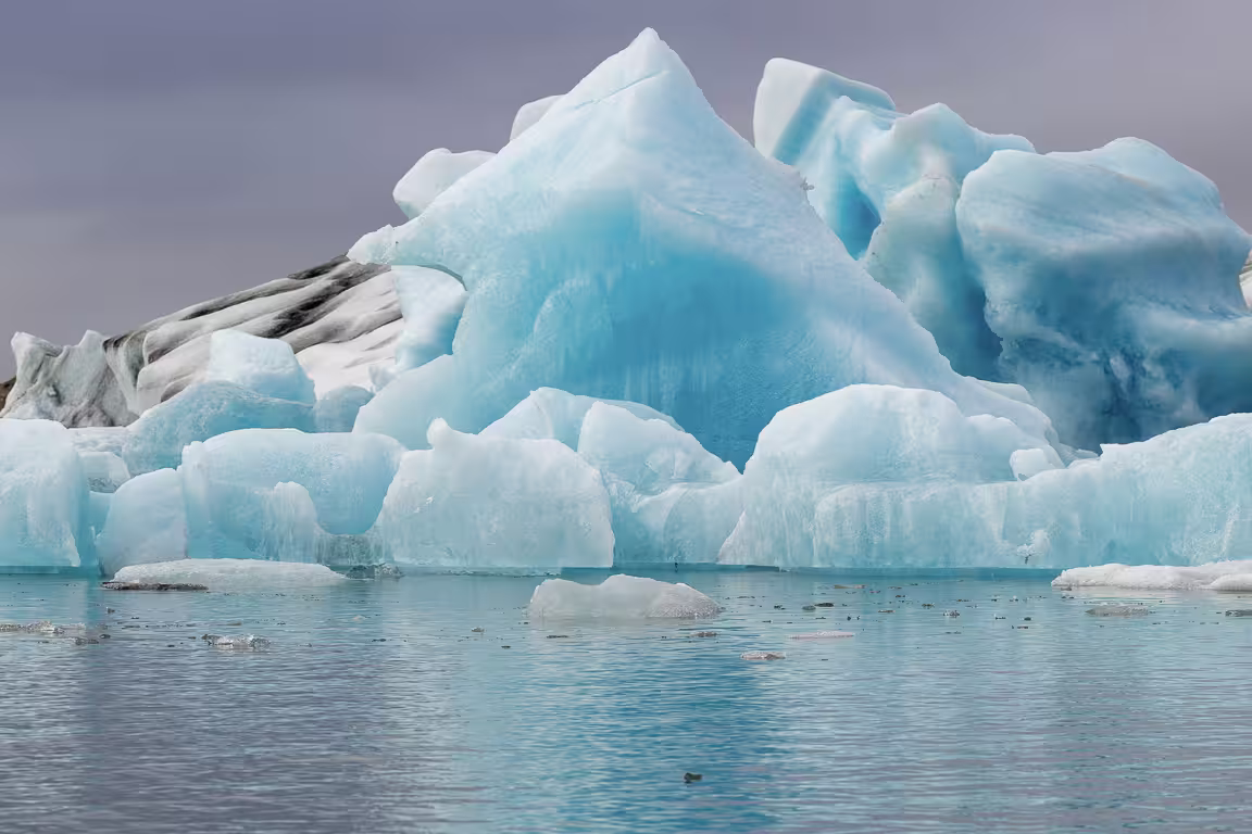 Vivid blue icebergs floating on glacial lagoon waters under overcast skies in Iceland