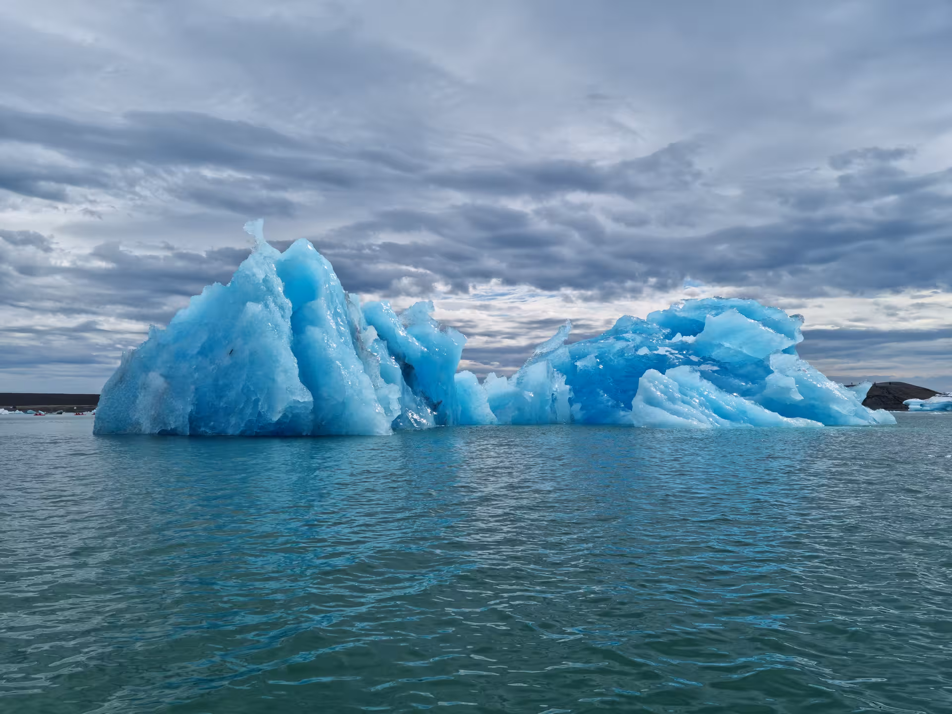 Vivid blue icebergs floating on calm glacial waters under a dramatic cloudy sky in Iceland