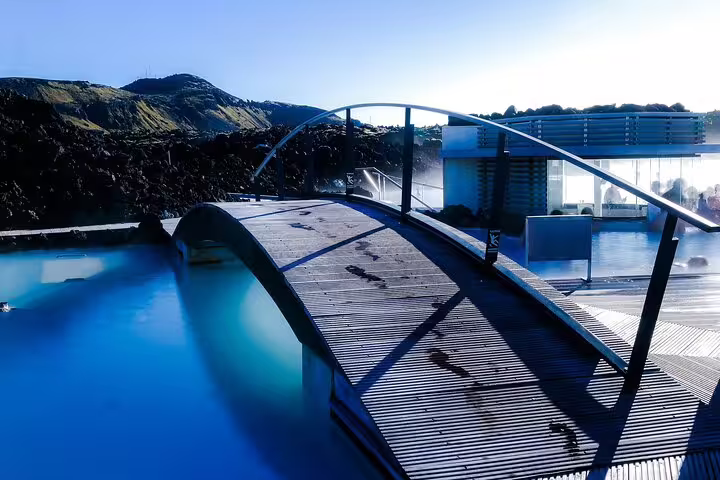 Wooden arched bridge over milky blue geothermal waters at Blue Lagoon Iceland with lava fields backdrop