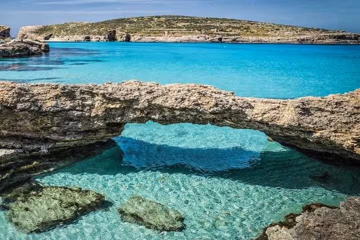 Natural rock arch over crystal-clear water at Comino Blue Lagoon, scenic stop on Malta to Gozo caves half-day tour