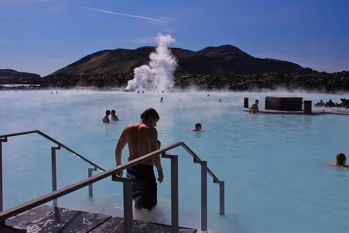 Visitors bathing in the milky blue geothermal waters of Blue Lagoon Iceland with steam rising in background