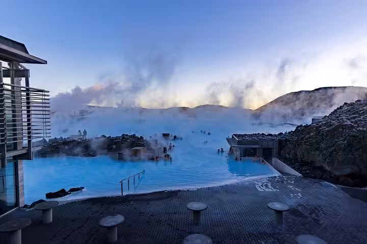Steaming Blue Lagoon geothermal pool in Iceland with bathers surrounded by lava rocks at dusk