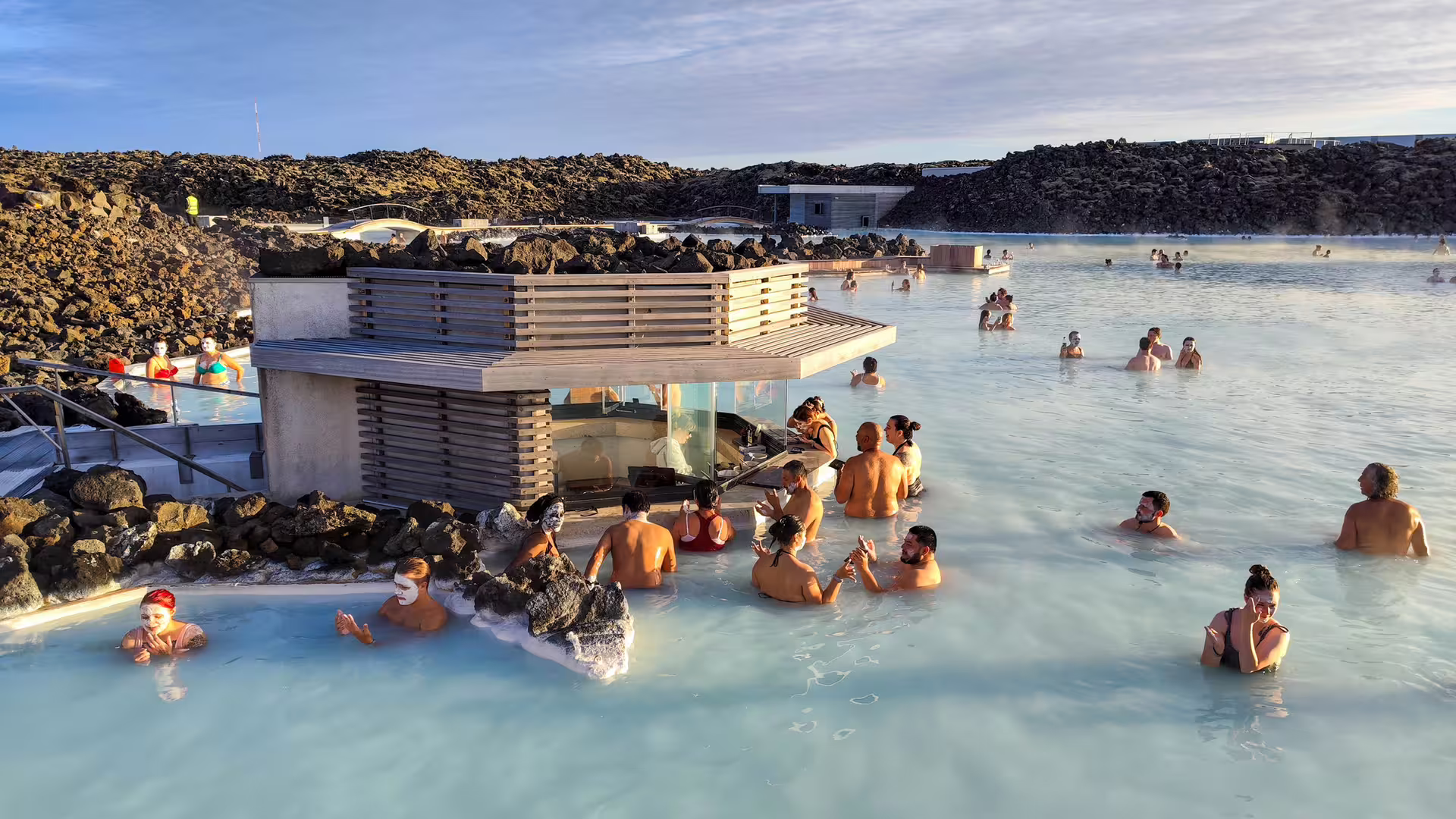 Tourists bathing in Blue Lagoon geothermal pool with milky blue waters and lava rock surroundings, Iceland