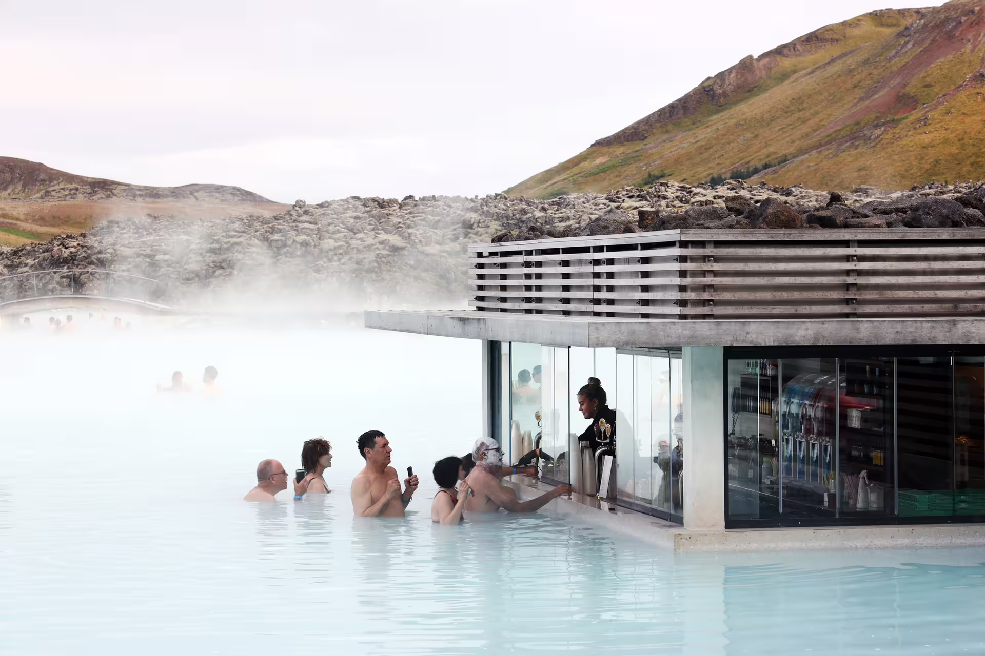 Bathers soaking in Blue Lagoon geothermal pool with in-water bar and steaming milky blue water, Iceland