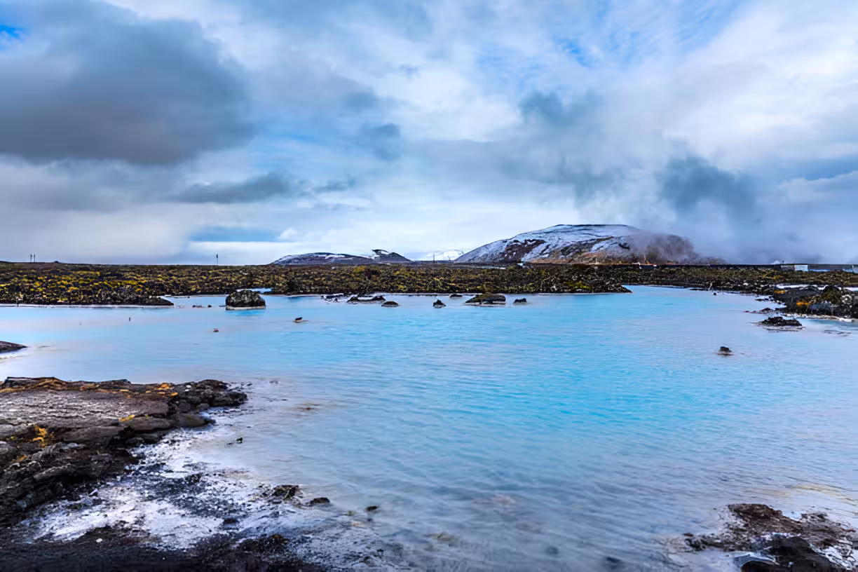 Blue Lagoon geothermal pool with milky turquoise water, lava rocks, and snow-capped hills in Iceland