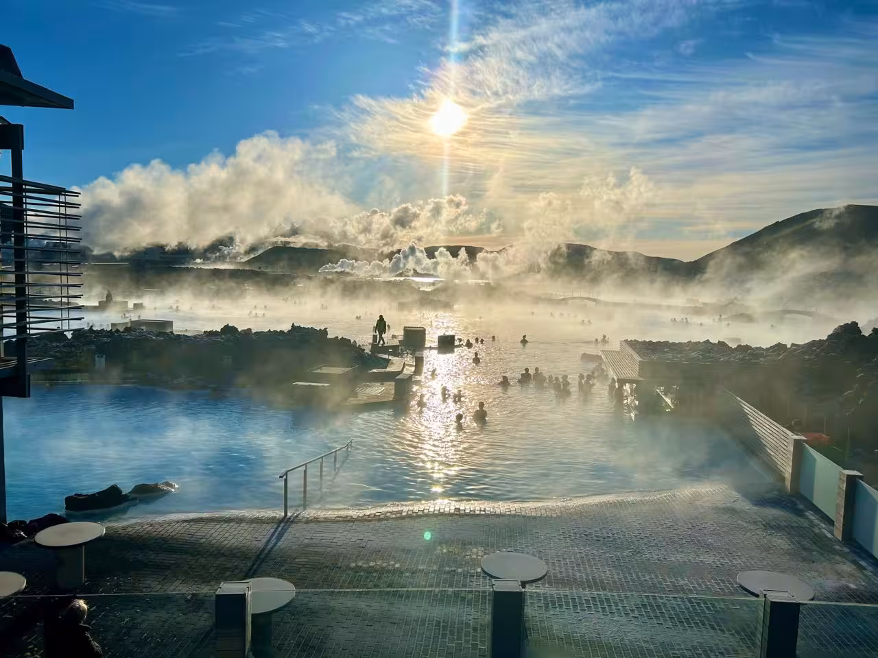 Steaming Blue Lagoon geothermal pool with bathers at sunset, surrounded by lava rocks in Iceland
