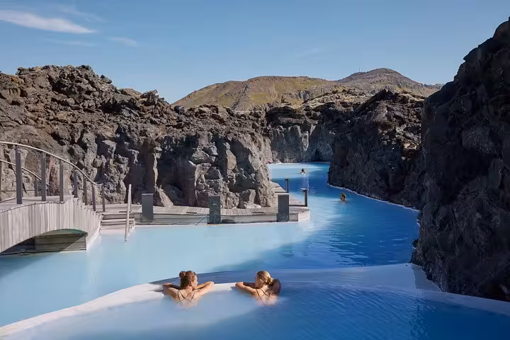 Two guests relaxing in the milky blue geothermal waters of the Blue Lagoon surrounded by volcanic rock