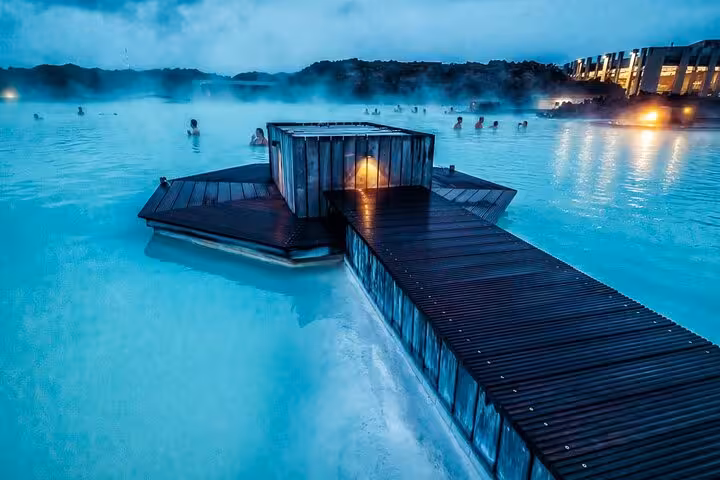 Steaming turquoise Blue Lagoon geothermal pool with wooden boardwalk and bathers at dusk, Iceland