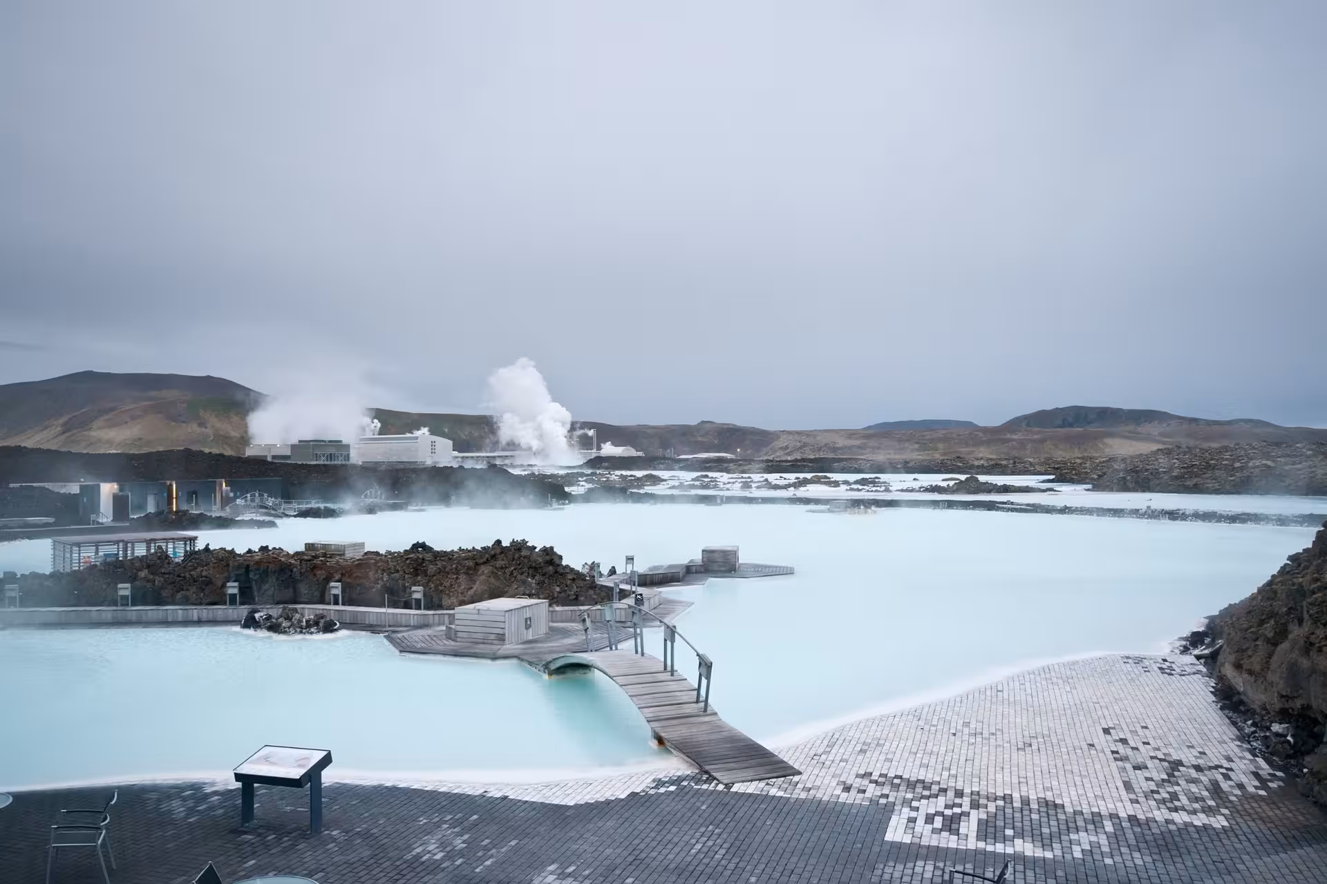Blue Lagoon geothermal spa with milky blue waters, wooden walkways, and steaming Svartsengi power plant in Iceland