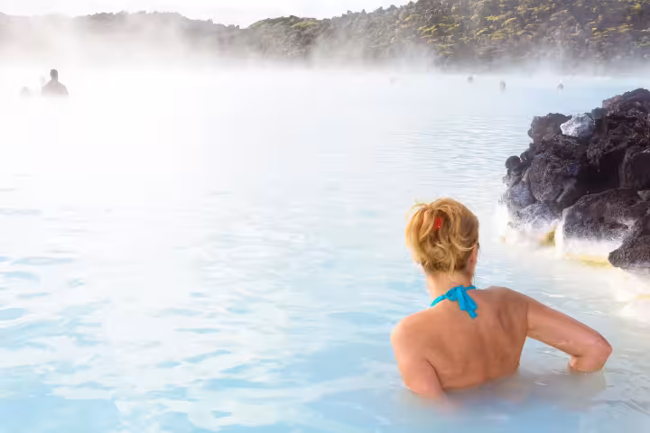 Woman relaxing in Blue Lagoon geothermal hot spring with steam rising over milky blue waters